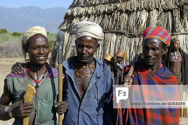 Three men of the Arbore people wearing different head dresses in front of a straw hut Weyto Ethiopia