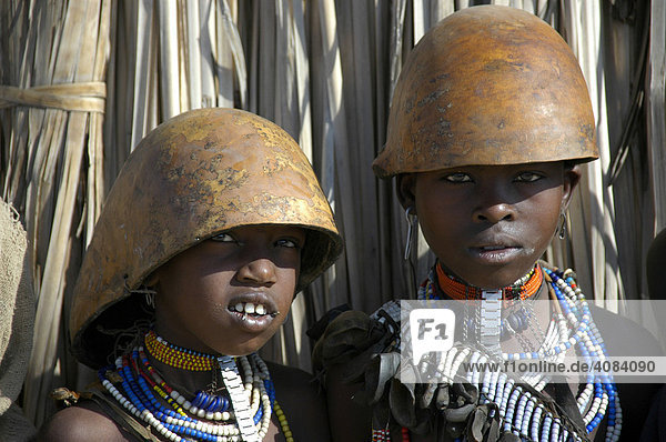 Two young girls of the Arbore people wearing colourful adornment with helmet calebasse in front of a straw hut near Weyto Ethiopia