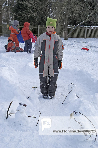 8-jähriger Junge steht zwischen kleinen Schneemännern