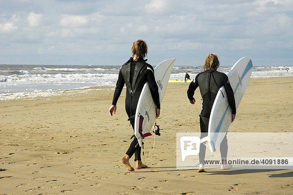 Zwei junge Maenner im Neoprenanzug tragen Surfbrett am Strand  Katwijk aan Zee  Südholland  Holland  Niederlande