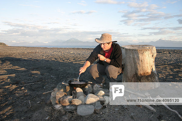 A woman cooks a steak on the open fire with a iron cast pan Homer Alaska USA