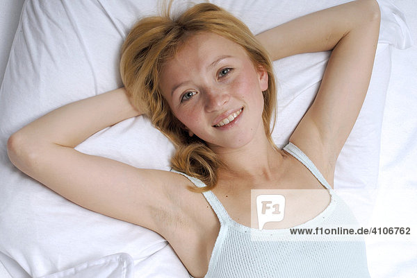 Porträt einer blonden  jungen Frau  liegt alleine im Bett