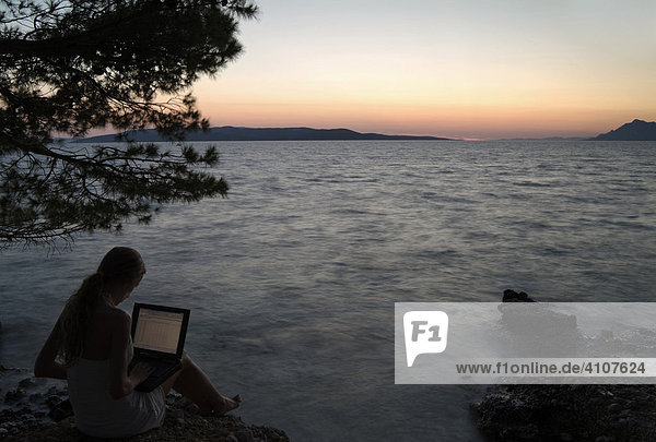Junge Frau mit Laptop an der Küste in der Dämmerung  Dalmatinische Küste  Kroatien  Europa.