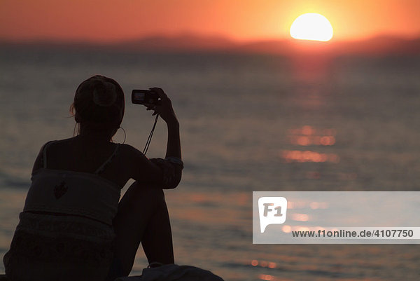 Frau fotografiert den Sonnenuntergang über dem Mittelmeer mit einer Digitalkamera