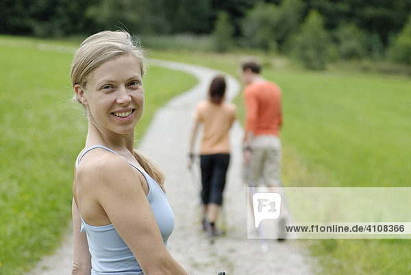 Junge Frau beim Nordic Walking hinter einem Pärchen