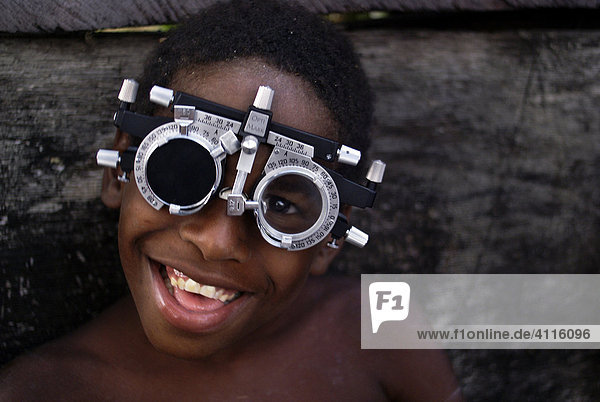 Lachender dunkelhäutiger Junge mit brillenähnlichem Sehtestgerät in einer Favela  Recife  Brasilien
