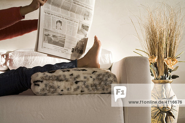 Frau liest mit hochgelegten Beinen die Zeitung