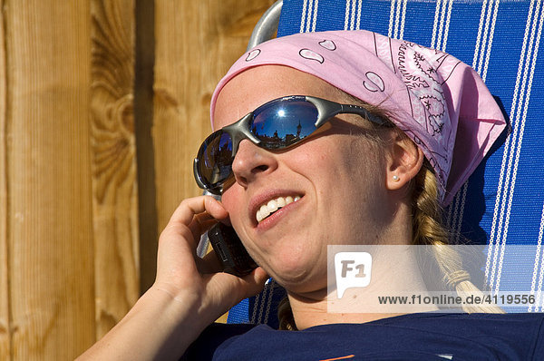 Junge Frau im Liegestuhl telefoniert mit dem Handy