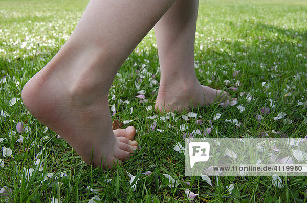 Young child walking barefoot in grass strewn with flower petals