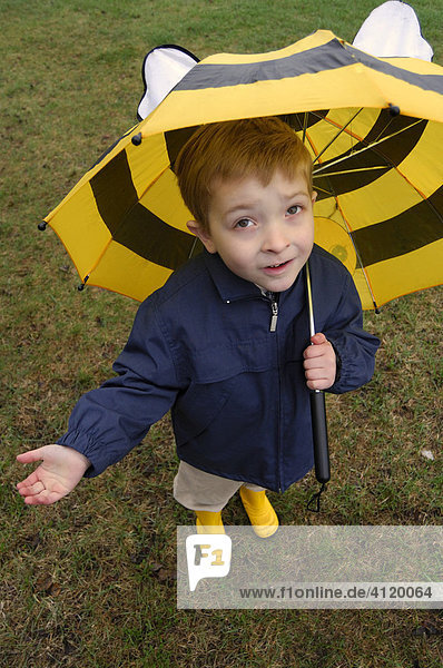 Young boy (age 5) with an umbrella and rain boots holding out his hand to see if it's raining