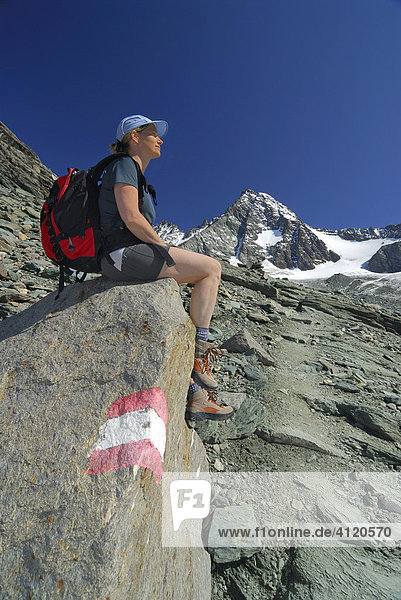 Frau sitzt neben einem Wanderweg vor dem Gipfel des Großglockner  Nationalpark Hohe Tauern  Tirol  Österreich