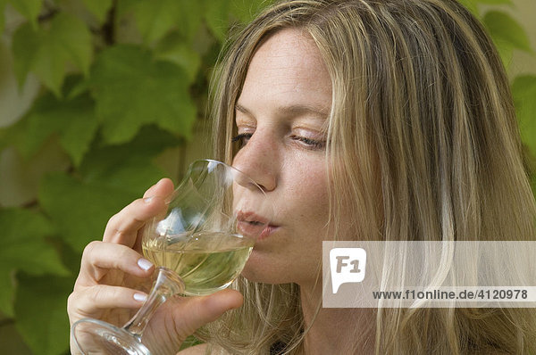 Blonde Frau trinkt ein Glas Weißwein  vor Weinlaub