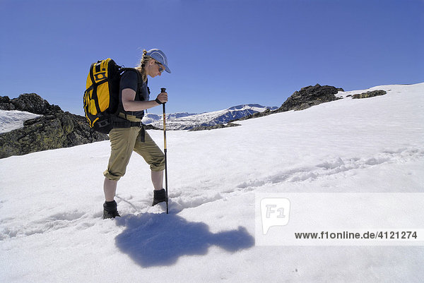 Woman wearing backpack trekking through a snowy field with poles  Jotunheimen National Park  Vaga  Oppland  Norway