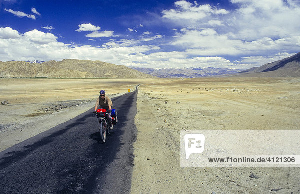 Reiseradfahrerin mit Kopftuch auf vollbepacktem Mountainbike auf einer einsamen Straße in der Hochgebirgswüste Ladakh  indischer Himalaya  Ladakh  Indien