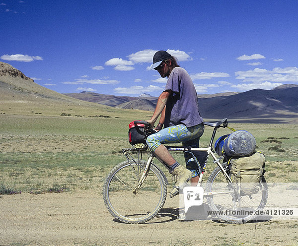 Cyclist on a fully-loaded mountain bike cycling along a dirt road  Himalayas  Ladakh  India