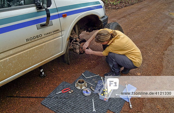 Frau repariert ein Vorderrad eines Geländewagens  auf einer Schotterstraße  Westaustralien  Australien