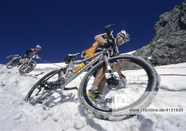 Zwei Teilnehmer der Adidas Bike Transalp Challenge  Mountainbikerennen  überqueren einen verschneiten Bergpass und tragen ihre Bikes über den Schnee hinunter  Pfunderer Joch  Südtirol  Italien  Europa
