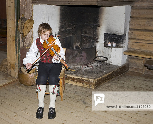 Violinspieler mit Hardanger-Fiedel vor Feuerstelle eines Hauses im Freilichtmuseum  Fagernes  Norwegen