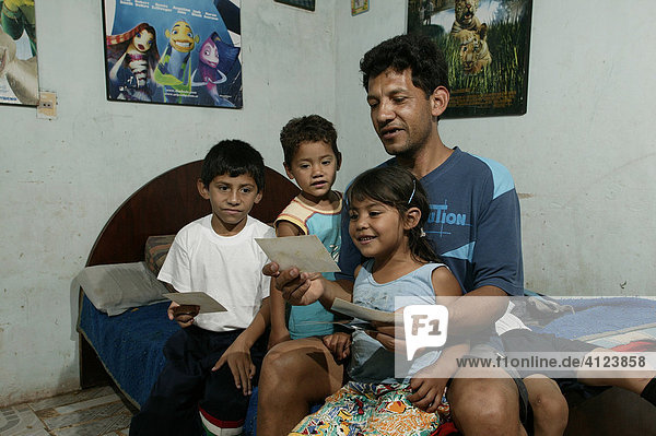 Guarani  father and children sitting on the bed and looking at pictures in the poor area of Chacarita  Asuncion  Paraguay  South America