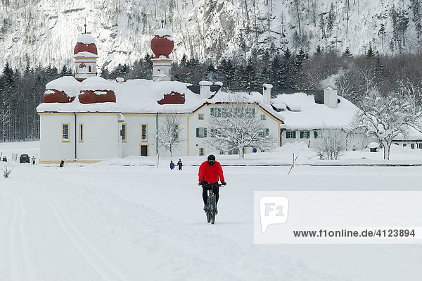 St. Bartholomä am zugefrorenen Königssee  Mountainbiker fährt über das Eis  Berchtesgadener Land  Oberbayern  Deutschland