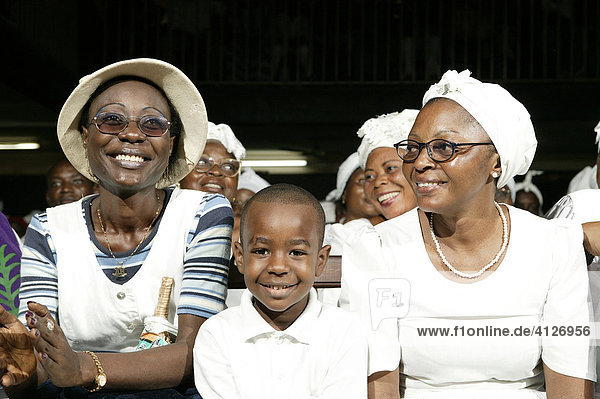 Smiling worshipers  young boy sitting between two women wearing glasses during a church service in Douala  Cameroon  Africa