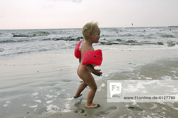 Little boy wearing swimming aids running along the beach  Caorle  Veneto  Italy