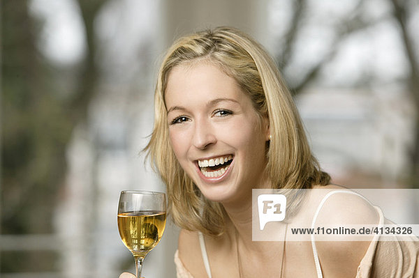 Junge blonde Frau trinkt Weißwein  lacht