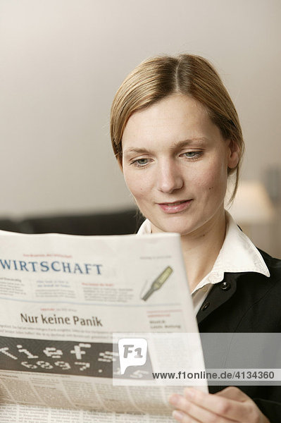 Junge blonde Frau mit Wirtschaftsteil einer Zeitung  lächelt