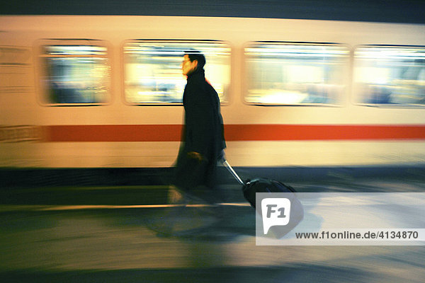 DEU Bundesrepublik Deutschland : Mann geht mit seinem Koffer Trolley auf einem Bahnsteig während ein Intercity Zug an ihm vorbei fährt.