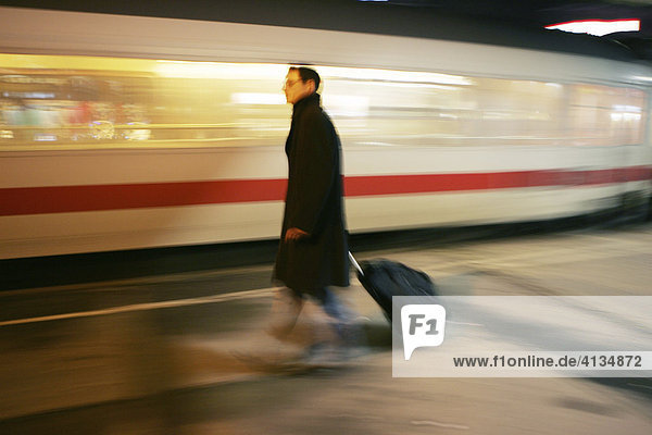 DEU Bundesrepublik Deutschland : Mann geht mit seinem Koffer Trolley auf einem Bahnsteig während ein Intercity Zug an ihm vorbei fährt.