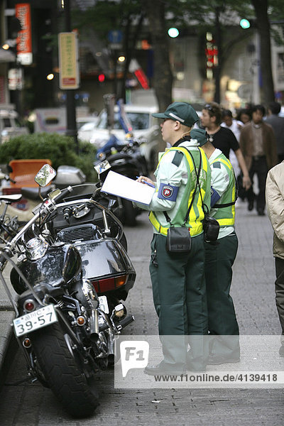 Parking enforcement officer writing a ticket for a motorcycle parked illegally on the sidewalk in Ginza  Tokyo  Japan  Asia
