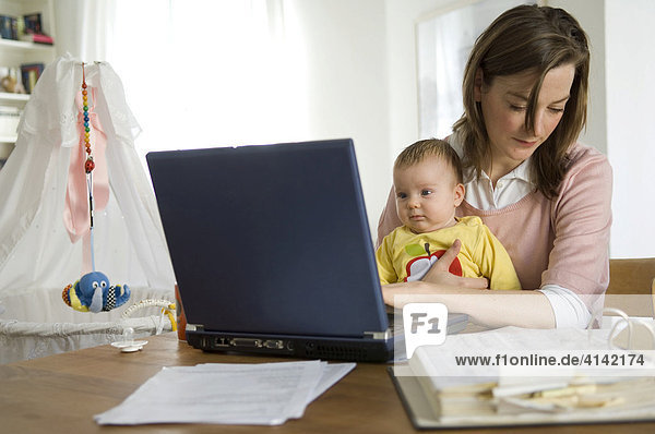 Junge Mutter mit Baby arbeitet zu Hause am Laptop