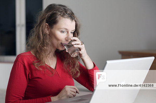 Junge Frau trinkt Wasser am PC