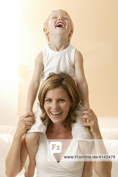 3-Jähriger Junge sitzt auf Mutters Schulter und lacht