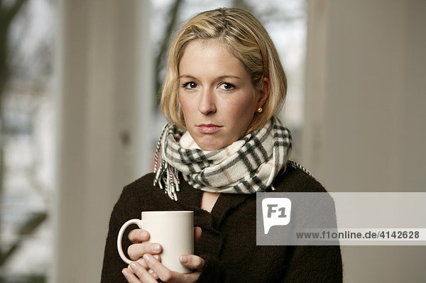 Junge Frau im dunklen Pullover mit Schal  mit Tasse