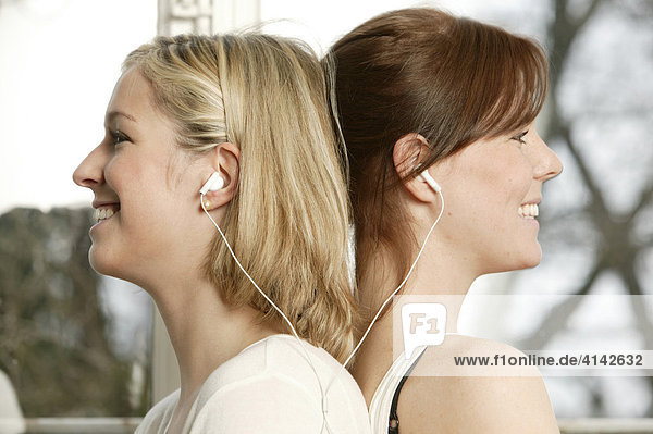Two young women sharing head phones to listen to music