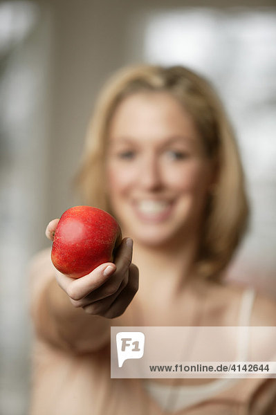 Junge  blonde Frau präsentiert roten Apfel  lächelt. Frau unscharf  selektive Schärfe
