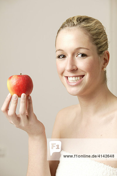 Junge  blonde Frau mit weissem Handtuch  mit Apfel  lächelt.