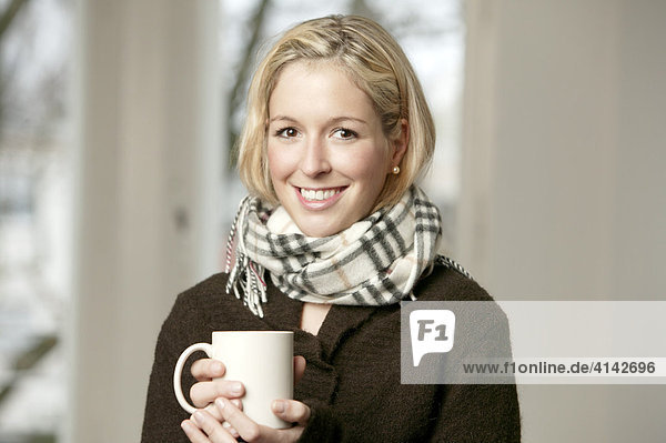 Junge Frau im dunklen Pullover mit Schal  mit Tasse  lächelt