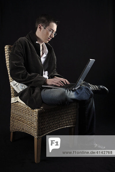 Junger Mann auf einem Stuhl sitzend und Laptop auf dem Schoss
