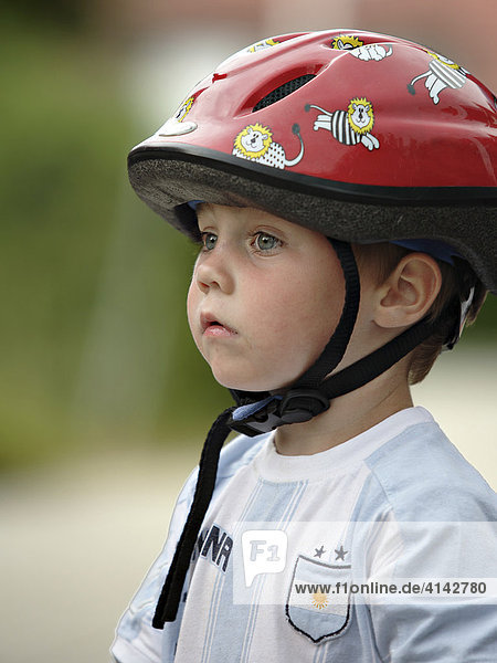 Ein kleiner Junge mit mit Fahrradhelm und Sportshirt mit nachdenklichem bzw. erstaunten Gesichtsausdruck