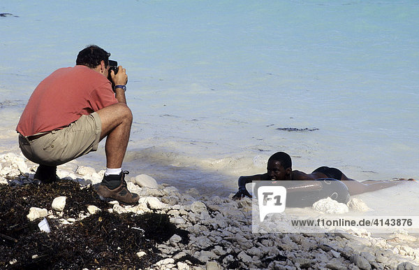 BHS  Bahamas  New Providence  Nassau: Tourist fotografiert einheimischen Jungen am Strand. Unabhängiger Staat der Westindischen Inseln und Mitglied des Commonwealth of Nations  Die Bahamas bestehen aus ueber 700 Inseln.