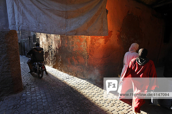 Motorcyclist driving and women walking through an alley in the historic Medina quarter of Marrakesh  Morocco  Africa