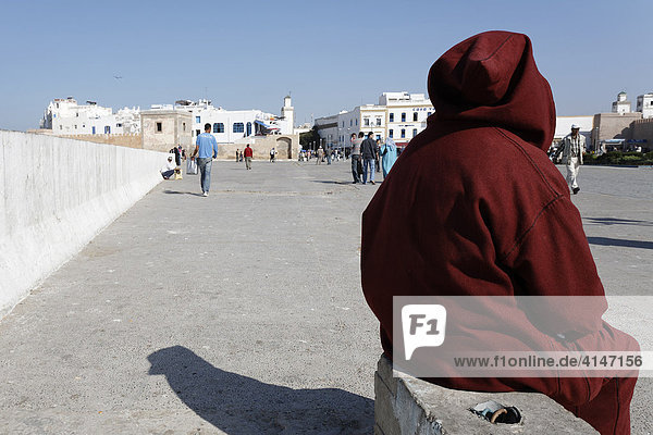 Mann in roter Djellaba ruht sich auf einer Steinbank aus  Place Moulay Hassan  Essaouira  Marokko  Afrika
