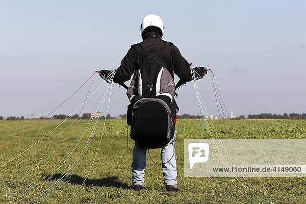 Gleitschirmflieger auf einem Feld in Startposition  hält die Fäden in der Hand  NRW  Deutschland