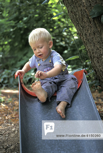 Zweijähriger Bub sitzt barfuß auf Rutsche