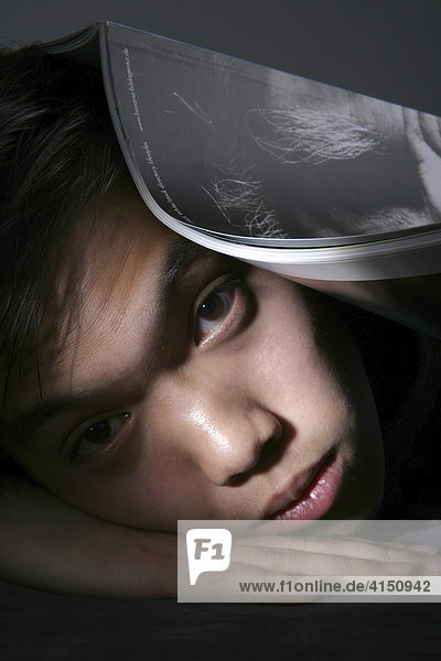Mann liegt erschöpft auf Hand gestützt mit Zeitschrift auf dem Kopf