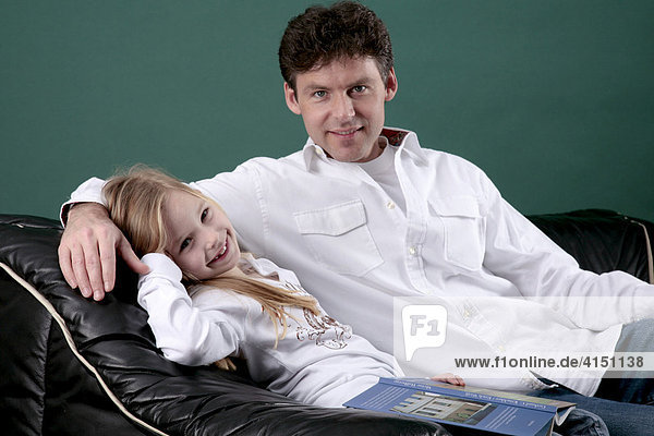 Vater und Tochter sitzen auf dem Sofa  die Tochter hat ein buch auf dem Schoß