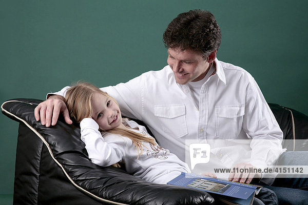 Vater und Tochter sitzen auf dem Sofa  die Tochter hat ein buch auf dem Schoß