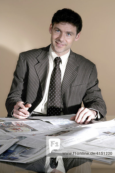Geschäftsmann sitzt vor vielen Zeitungen